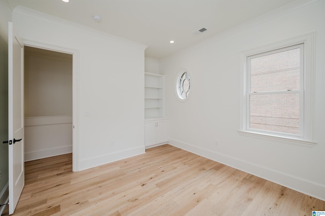 empty room featuring crown molding, built in features, and light hardwood / wood-style floors