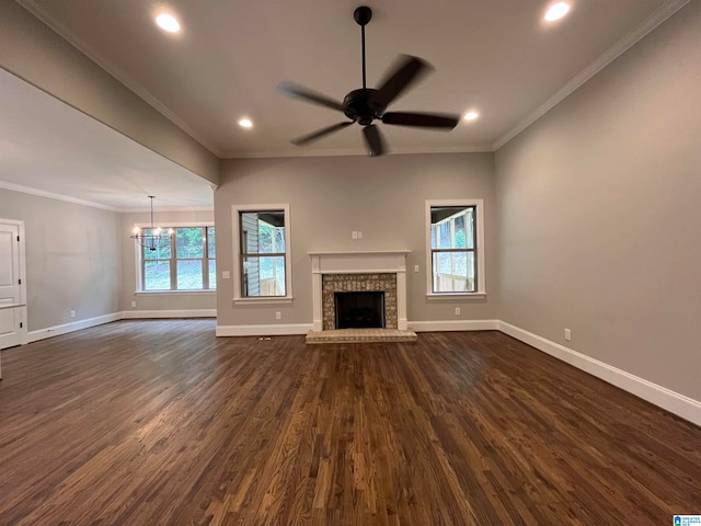 unfurnished living room featuring dark hardwood / wood-style flooring, ceiling fan with notable chandelier, a brick fireplace, and crown molding