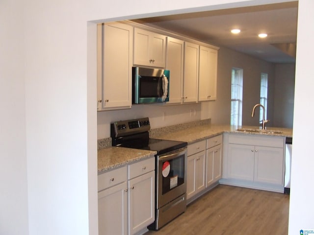 kitchen featuring light wood-type flooring, white cabinets, light stone counters, appliances with stainless steel finishes, and sink