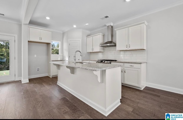 kitchen featuring sink, white cabinets, a center island with sink, and wall chimney range hood