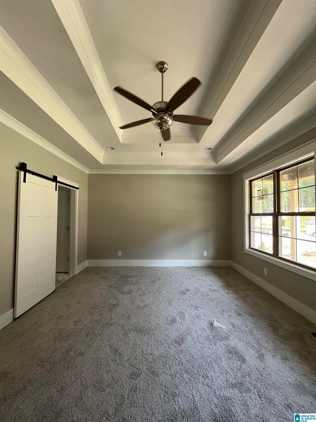 unfurnished bedroom featuring carpet floors, ceiling fan, ornamental molding, a tray ceiling, and a barn door