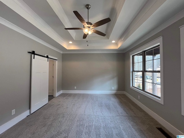 unfurnished bedroom featuring a barn door, dark carpet, a tray ceiling, and ornamental molding