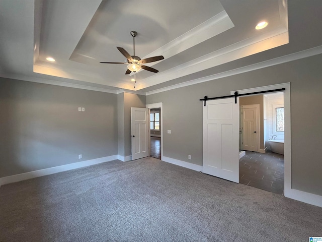 unfurnished bedroom featuring a barn door, a raised ceiling, and dark colored carpet