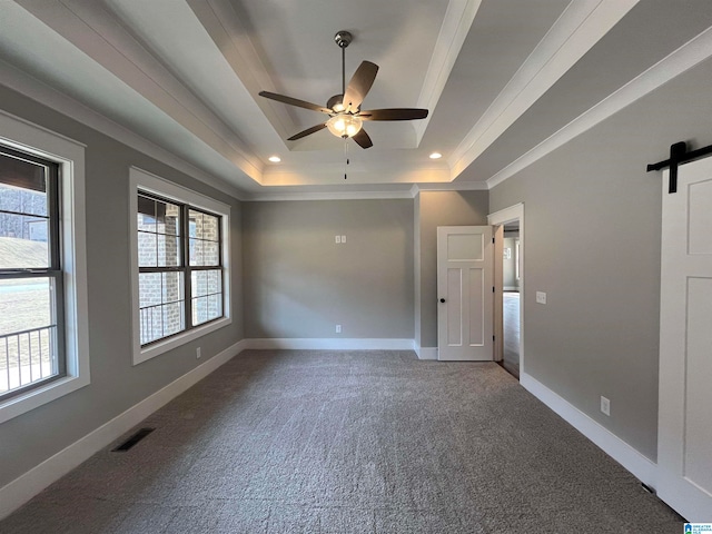 empty room featuring a tray ceiling, ceiling fan, a barn door, carpet flooring, and crown molding