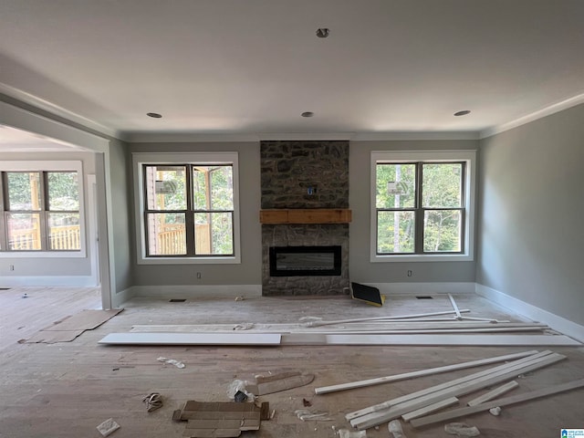 unfurnished living room with a stone fireplace, crown molding, light hardwood / wood-style floors, and plenty of natural light