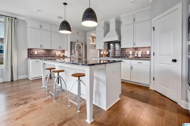 kitchen with light hardwood / wood-style flooring, premium range hood, an island with sink, and backsplash