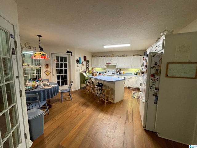 kitchen with hardwood / wood-style flooring, white cabinetry, white appliances, hanging light fixtures, and a kitchen breakfast bar