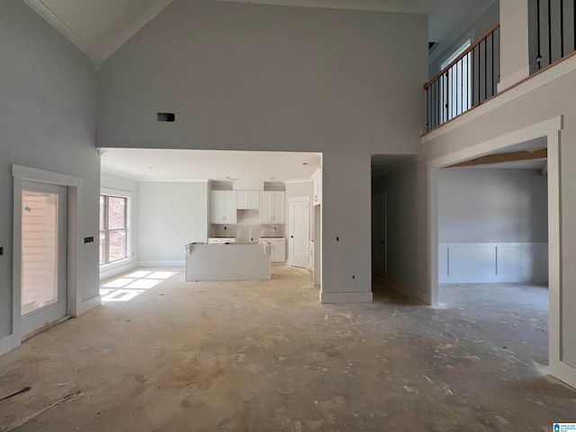 unfurnished living room featuring ornamental molding and high vaulted ceiling