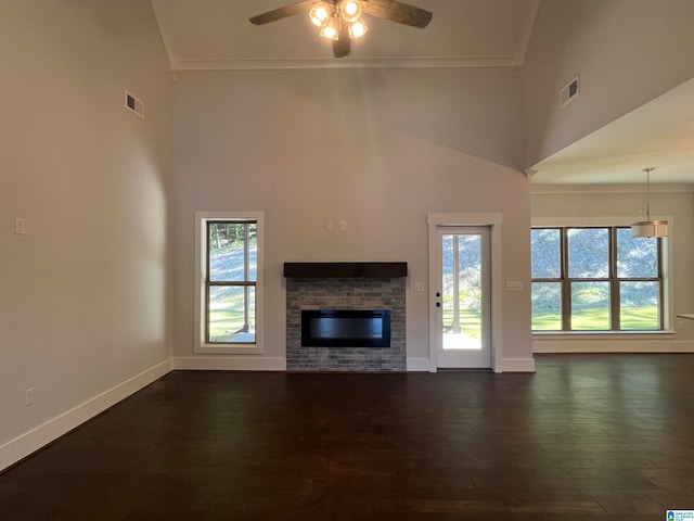 unfurnished living room with ceiling fan, a healthy amount of sunlight, a stone fireplace, and dark wood-type flooring