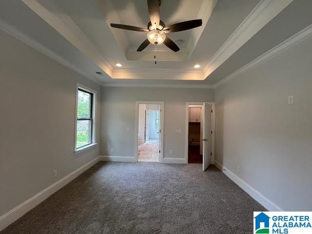 unfurnished bedroom with ensuite bath, ceiling fan, ornamental molding, a tray ceiling, and carpet floors