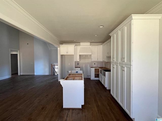 kitchen with dark wood-type flooring, sink, ornamental molding, a kitchen island, and white cabinetry