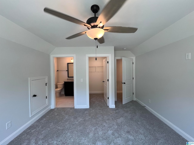 unfurnished bedroom featuring carpet flooring, a walk in closet, vaulted ceiling, and ceiling fan