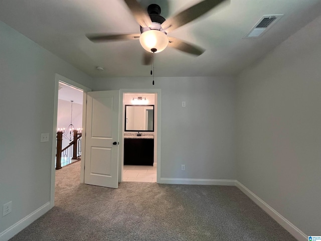 unfurnished bedroom featuring carpet, ceiling fan with notable chandelier, sink, and ensuite bathroom