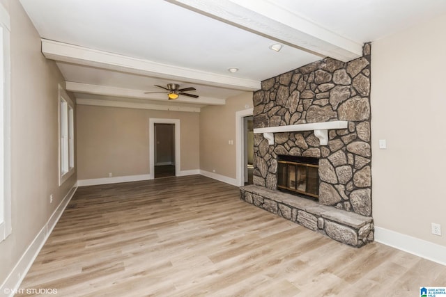 unfurnished living room featuring a fireplace, beam ceiling, ceiling fan, and light wood-type flooring