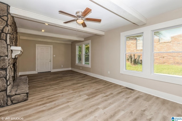 unfurnished living room featuring beam ceiling, a stone fireplace, ceiling fan, and light hardwood / wood-style flooring