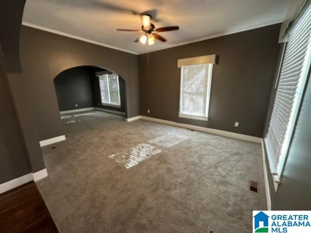 unfurnished room featuring ceiling fan, ornamental molding, and dark colored carpet