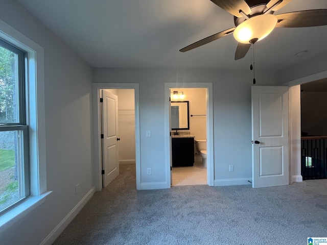 unfurnished bedroom featuring light carpet, a walk in closet, ensuite bathroom, and ceiling fan