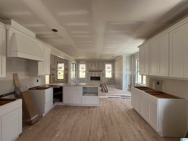 kitchen with custom range hood, light wood-type flooring, and white cabinetry