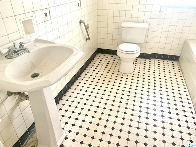 bathroom with tile flooring, toilet, and tile walls