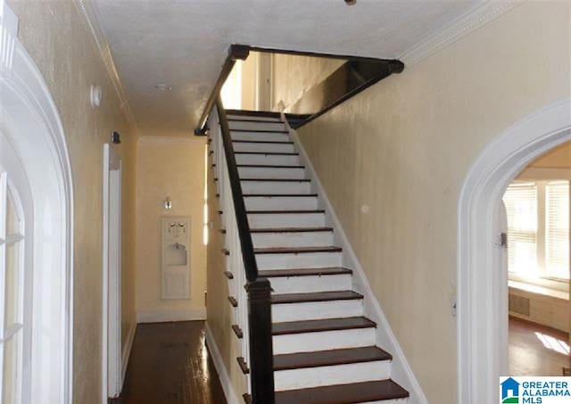 stairs featuring crown molding and dark wood-type flooring