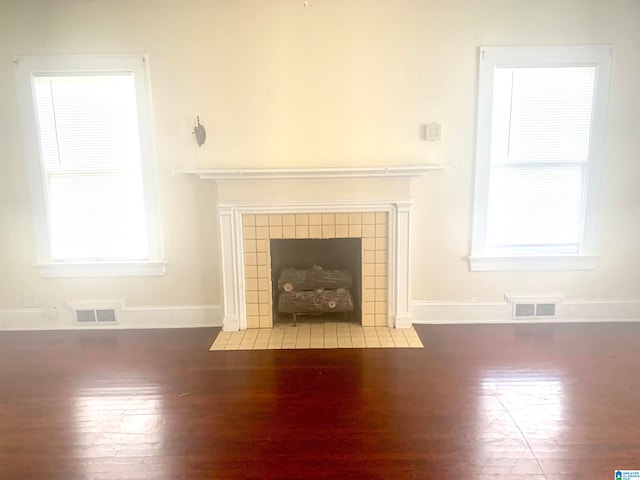 unfurnished living room featuring a tiled fireplace and dark hardwood / wood-style flooring