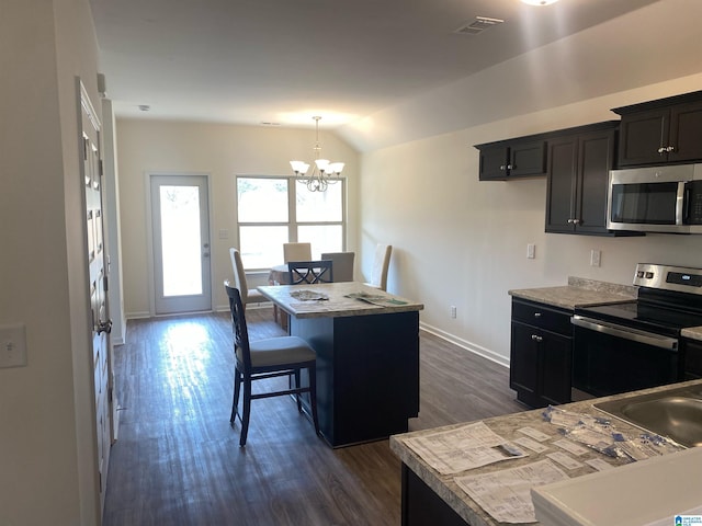 kitchen featuring dark wood-type flooring, vaulted ceiling, appliances with stainless steel finishes, a notable chandelier, and a kitchen island