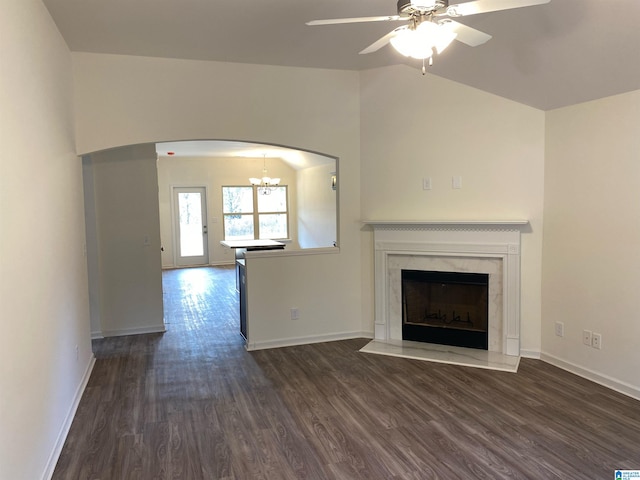 unfurnished living room featuring ceiling fan with notable chandelier, a premium fireplace, dark wood-type flooring, and vaulted ceiling