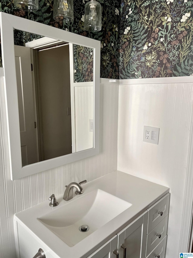 bathroom featuring wallpapered walls, vanity, and wainscoting