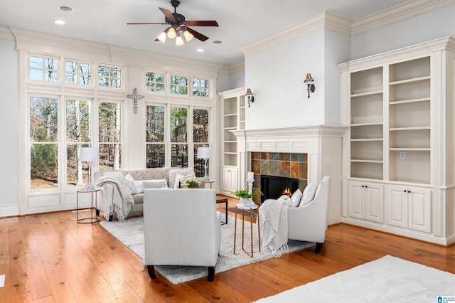 living room with a tile fireplace, ceiling fan, crown molding, and hardwood / wood-style flooring