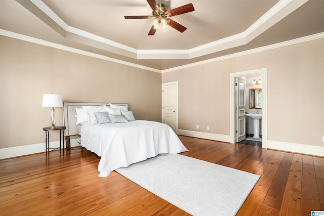 bedroom with a tray ceiling, connected bathroom, crown molding, and ceiling fan