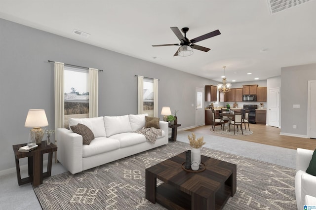 carpeted living room featuring ceiling fan with notable chandelier