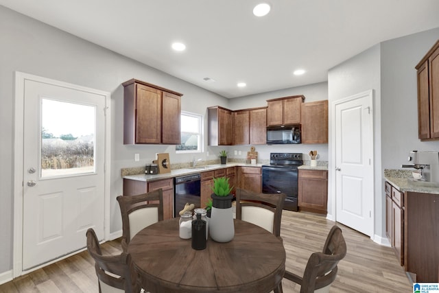 kitchen featuring a healthy amount of sunlight, light hardwood / wood-style floors, light stone counters, and black appliances