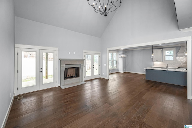 unfurnished living room with a chandelier, plenty of natural light, high vaulted ceiling, dark hardwood / wood-style floors, and a premium fireplace