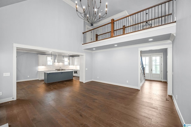 unfurnished living room with sink, french doors, a chandelier, high vaulted ceiling, and dark wood-type flooring