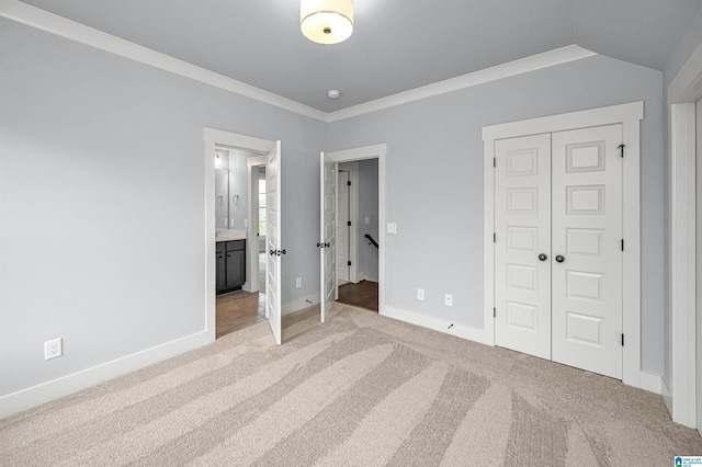 unfurnished bedroom featuring a closet, ensuite bath, crown molding, light colored carpet, and lofted ceiling