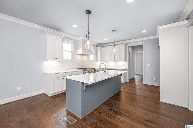 kitchen featuring tasteful backsplash, a center island with sink, light stone counters, dark hardwood / wood-style floors, and white cabinetry