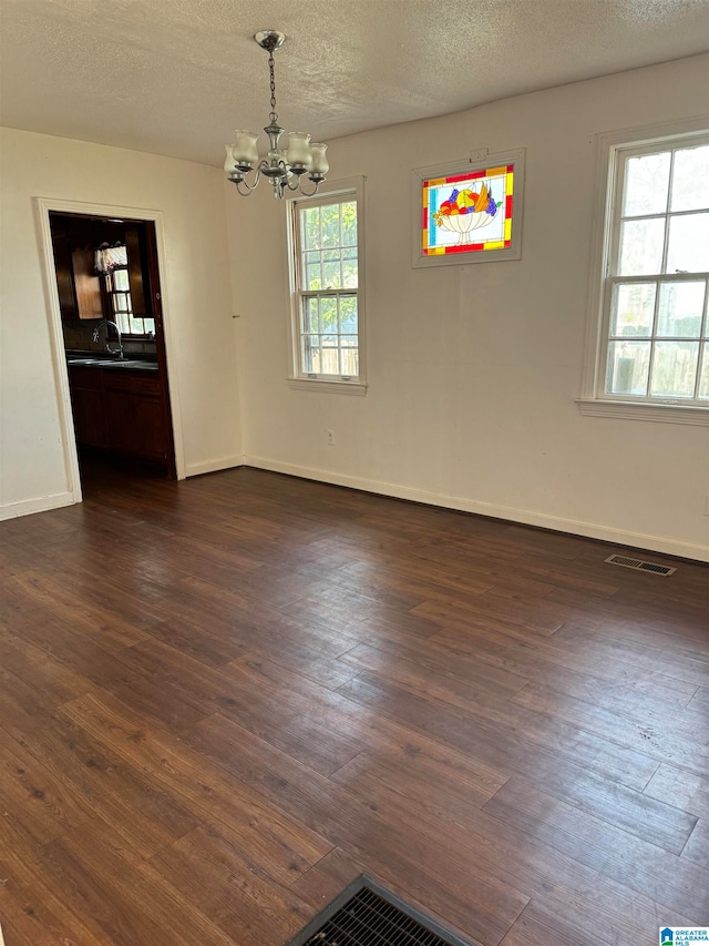 empty room with a chandelier, a textured ceiling, dark hardwood / wood-style floors, and a healthy amount of sunlight