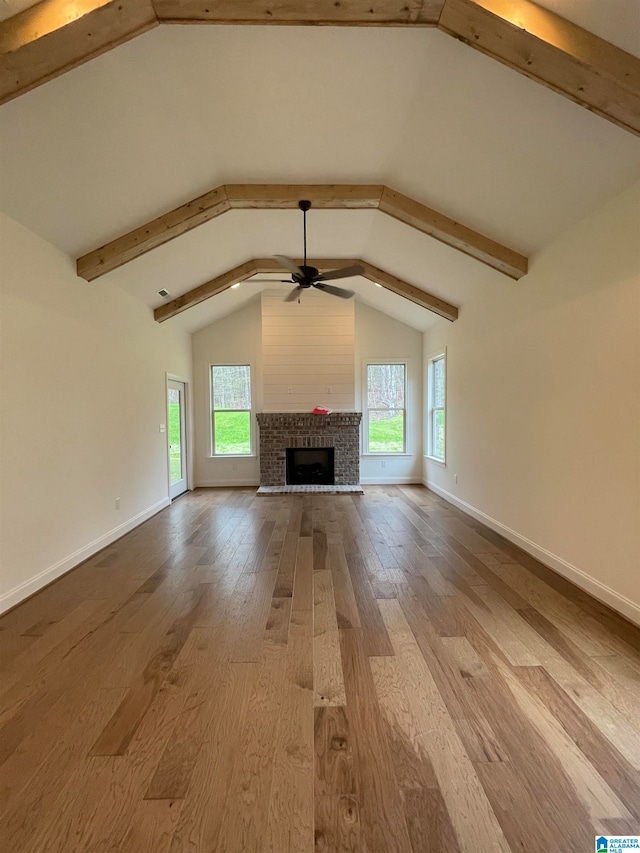 unfurnished living room with dark wood-type flooring, a brick fireplace, ceiling fan, and vaulted ceiling with beams