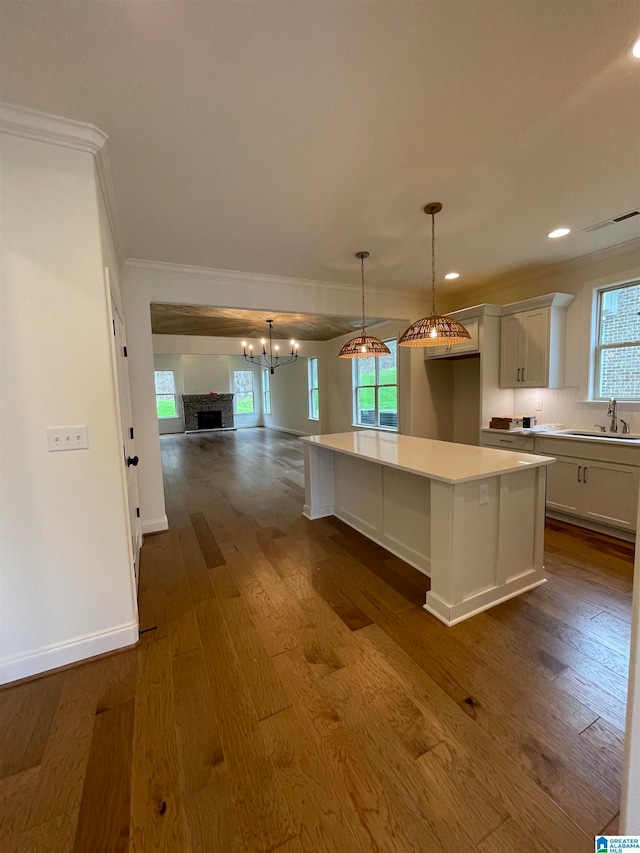 kitchen with a kitchen island, hanging light fixtures, dark wood-type flooring, white cabinets, and sink