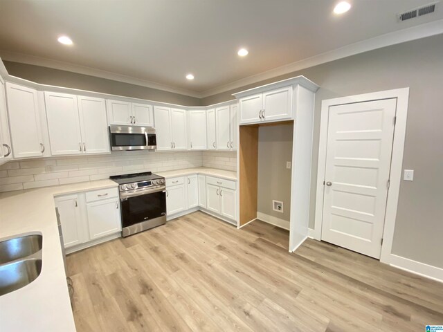 kitchen featuring light wood-type flooring, white cabinetry, ornamental molding, appliances with stainless steel finishes, and tasteful backsplash