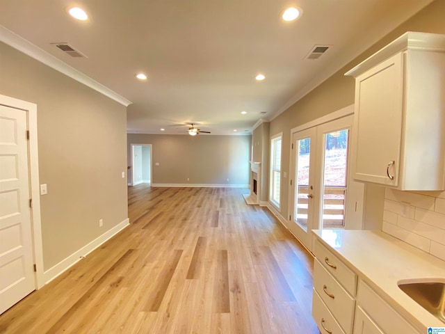 interior space featuring ornamental molding, light hardwood / wood-style floors, tasteful backsplash, and white cabinetry