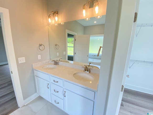 bathroom featuring hardwood / wood-style floors, a bath, vanity with extensive cabinet space, and double sink