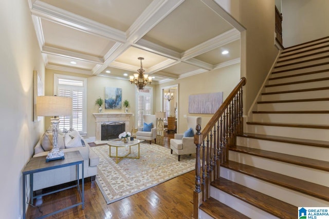 living room featuring coffered ceiling, dark wood-type flooring, a chandelier, beamed ceiling, and ornamental molding