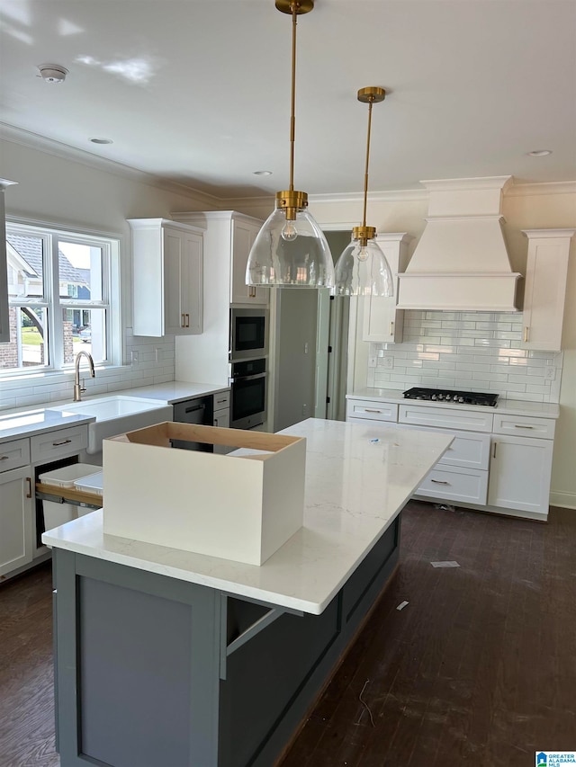 kitchen with appliances with stainless steel finishes, custom range hood, a center island, white cabinetry, and hanging light fixtures