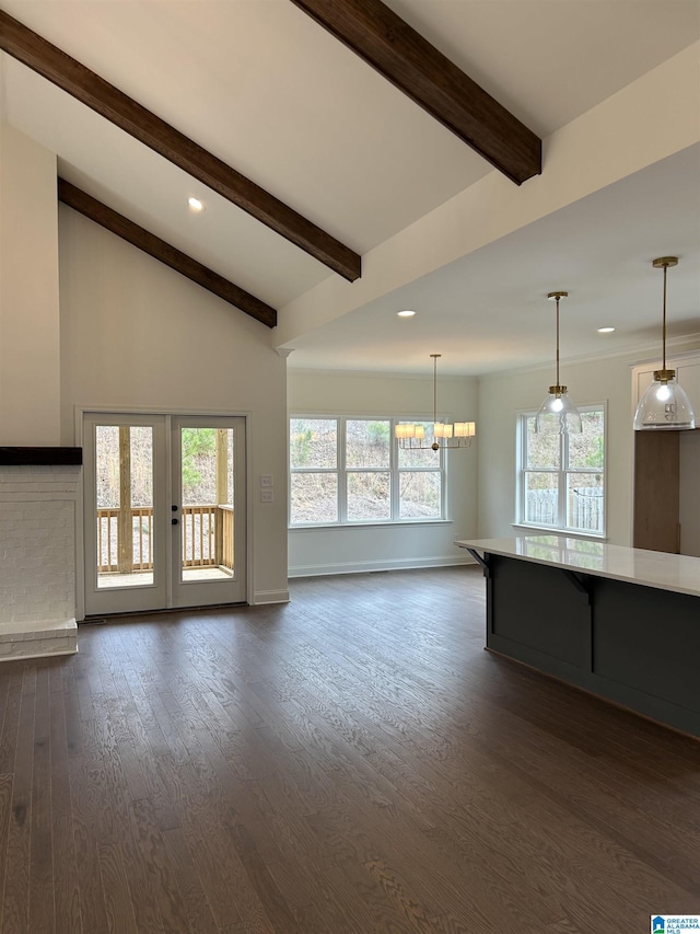 unfurnished living room featuring vaulted ceiling with beams, a healthy amount of sunlight, dark wood-type flooring, and a chandelier