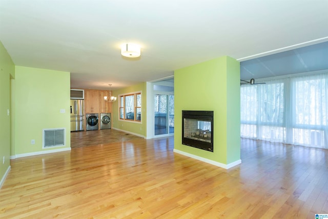 unfurnished living room with a multi sided fireplace, a notable chandelier, independent washer and dryer, and light hardwood / wood-style flooring