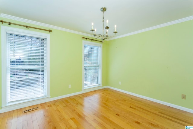 empty room featuring ornamental molding, plenty of natural light, hardwood / wood-style floors, and an inviting chandelier