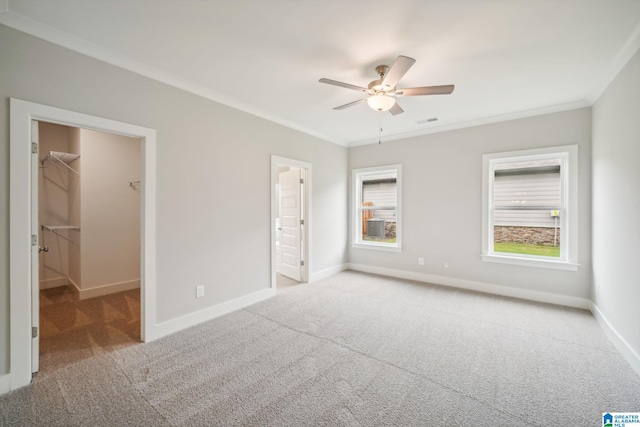 unfurnished bedroom with ceiling fan, a walk in closet, crown molding, and multiple windows