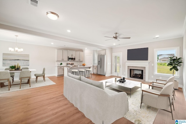 living room with ceiling fan with notable chandelier, light hardwood / wood-style flooring, and crown molding