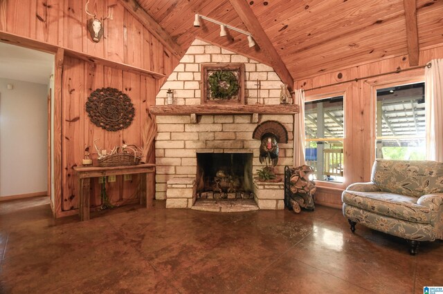 living room with a stone fireplace, beam ceiling, wood ceiling, track lighting, and wood walls